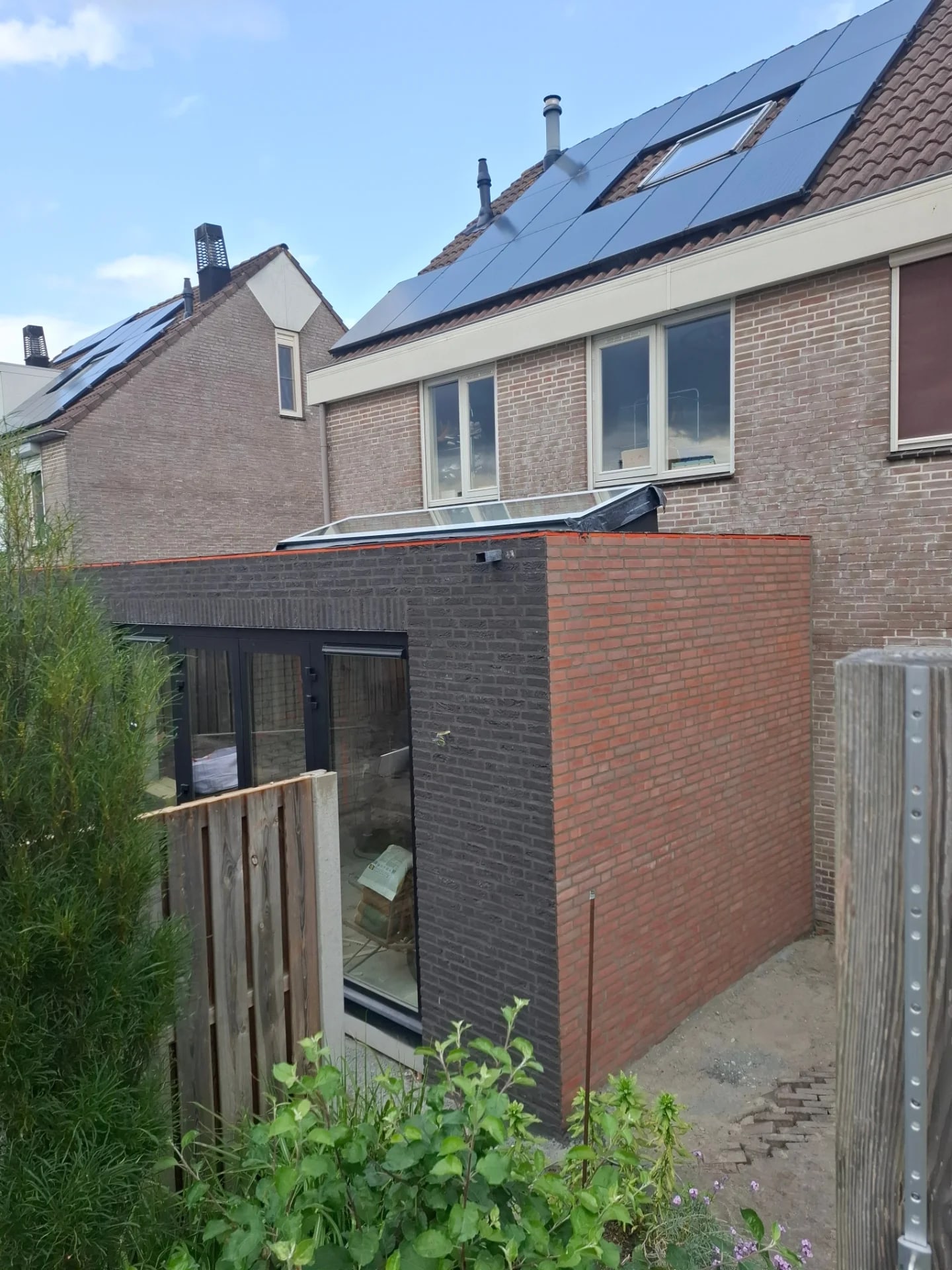 Aanbouw met een antraciet gevel en een zijwand in rode steen, met een lichtstraat op het dak