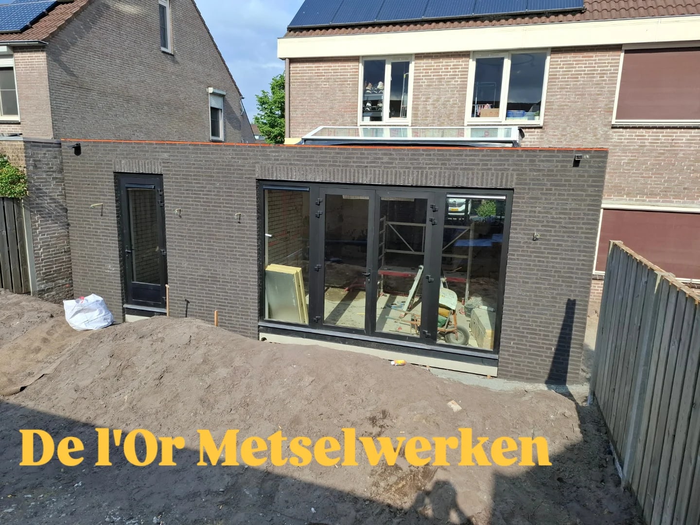 Nieuwe aanbouw in antraciet steen met grote glazen schuifpui aan de achterkant van een rijtjeshuis