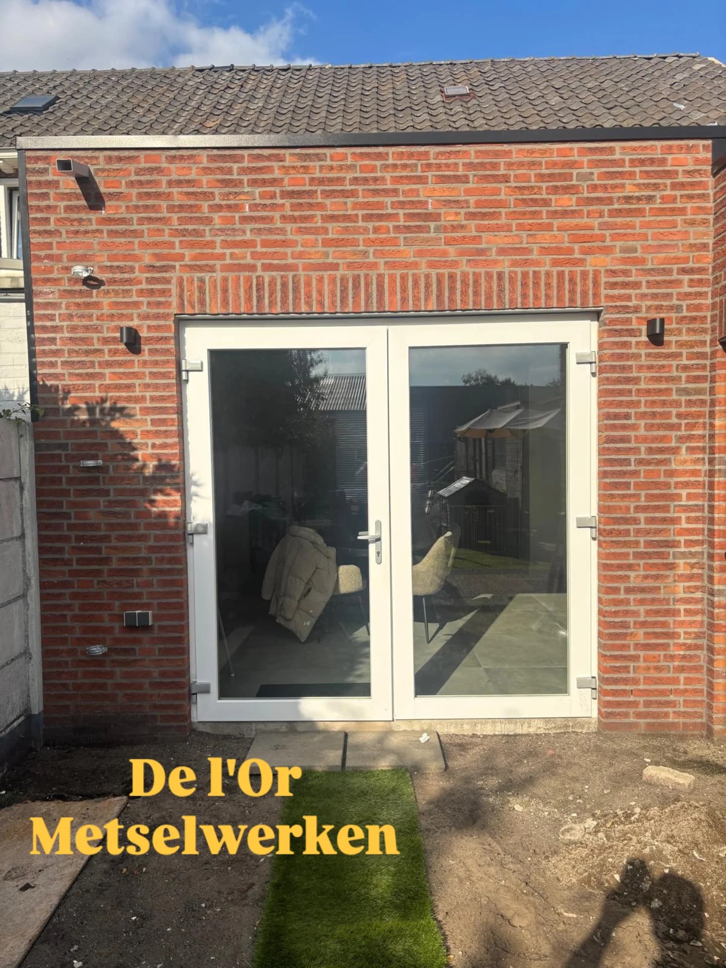 Gemetselde aanbouw in rode steen met witte openslaande tuindeuren