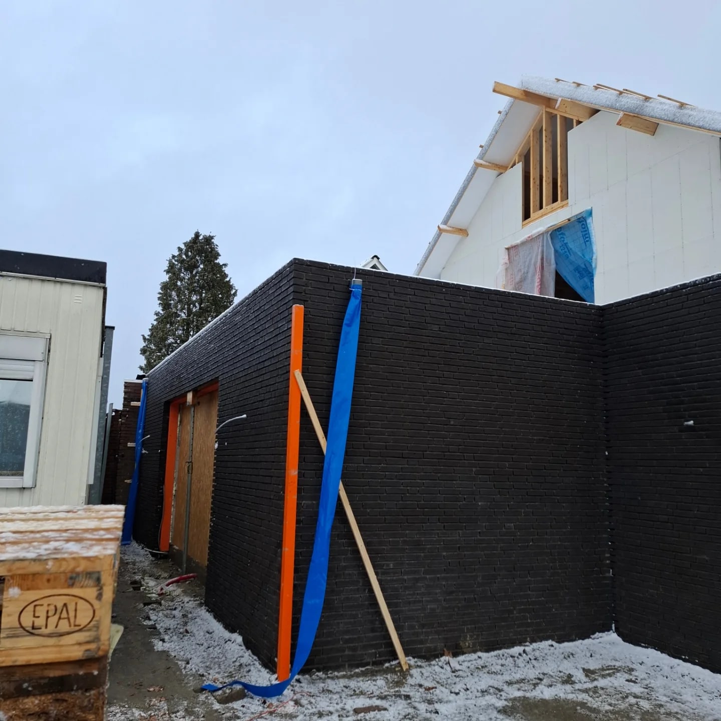 Aanbouw in zwarte steen in aanbouw achter een woning, met afdekfolie op de vensterbanken