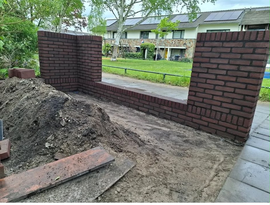 Nieuw gemetselde tuinmuur in donkerrode steen met twee hogere penanten bij een voortuin
