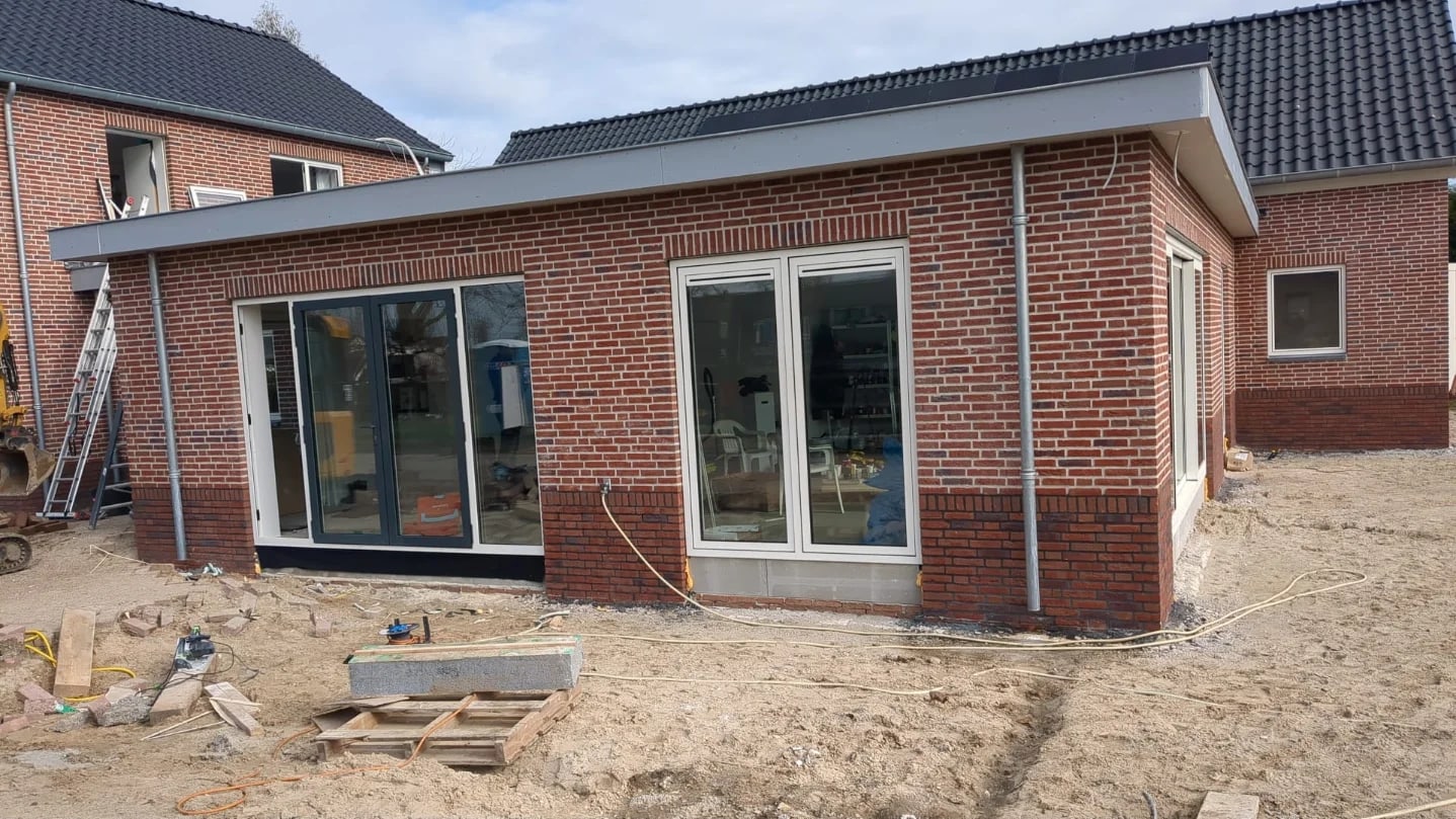 Achterzijde van een nieuw woonhuis met een gemetselde uitbouw en grote glazen puien