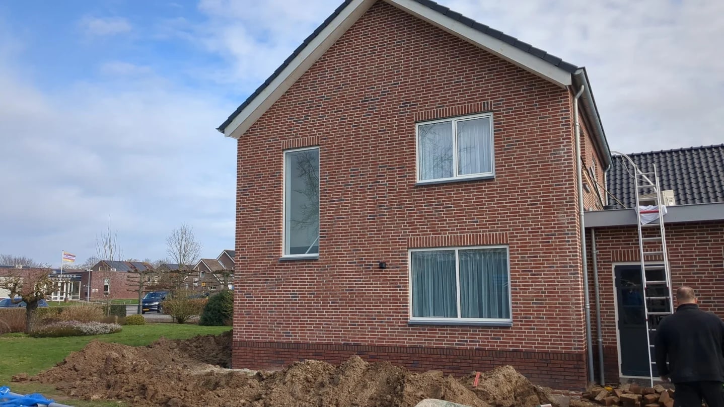 Nieuw gemetseld woonhuis in rode steen met een donkere plint en witte kozijnen in Velddriel