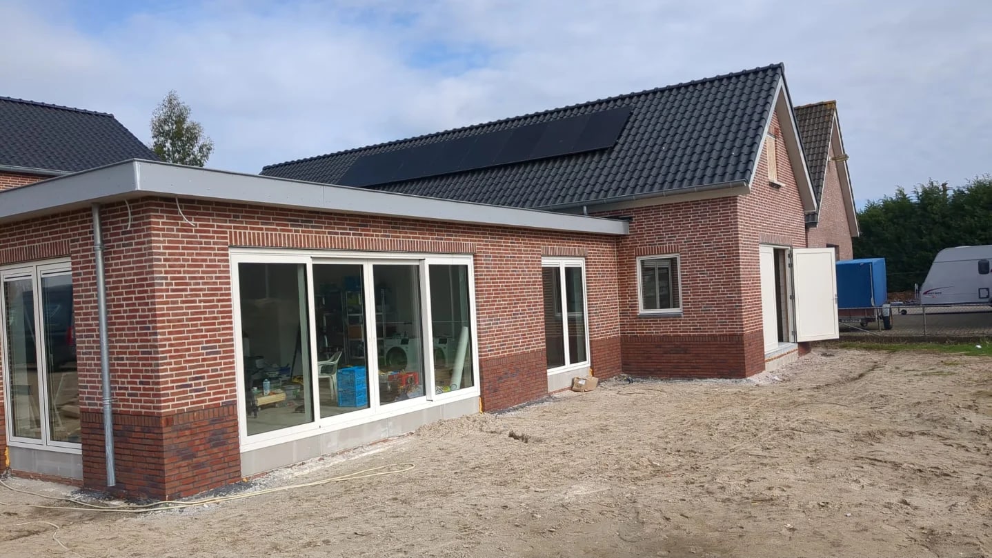 Zijkant van een nieuw woonhuis in rode steen met een brede glazen pui